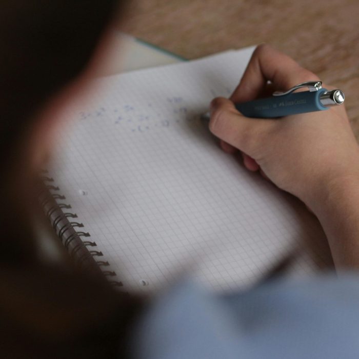 A student writes mathematical notes in a notebook using a pen, focus on studying.